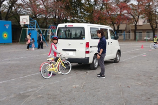 車のそばで自転車の安全確認を行う児童の写真